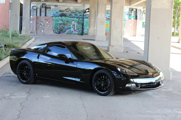 Black Corvette C6 after paint correction and coating, parked under a mural