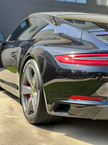 Rear quarter of a black Porsche 911 after coating, reflecting the yard behind it